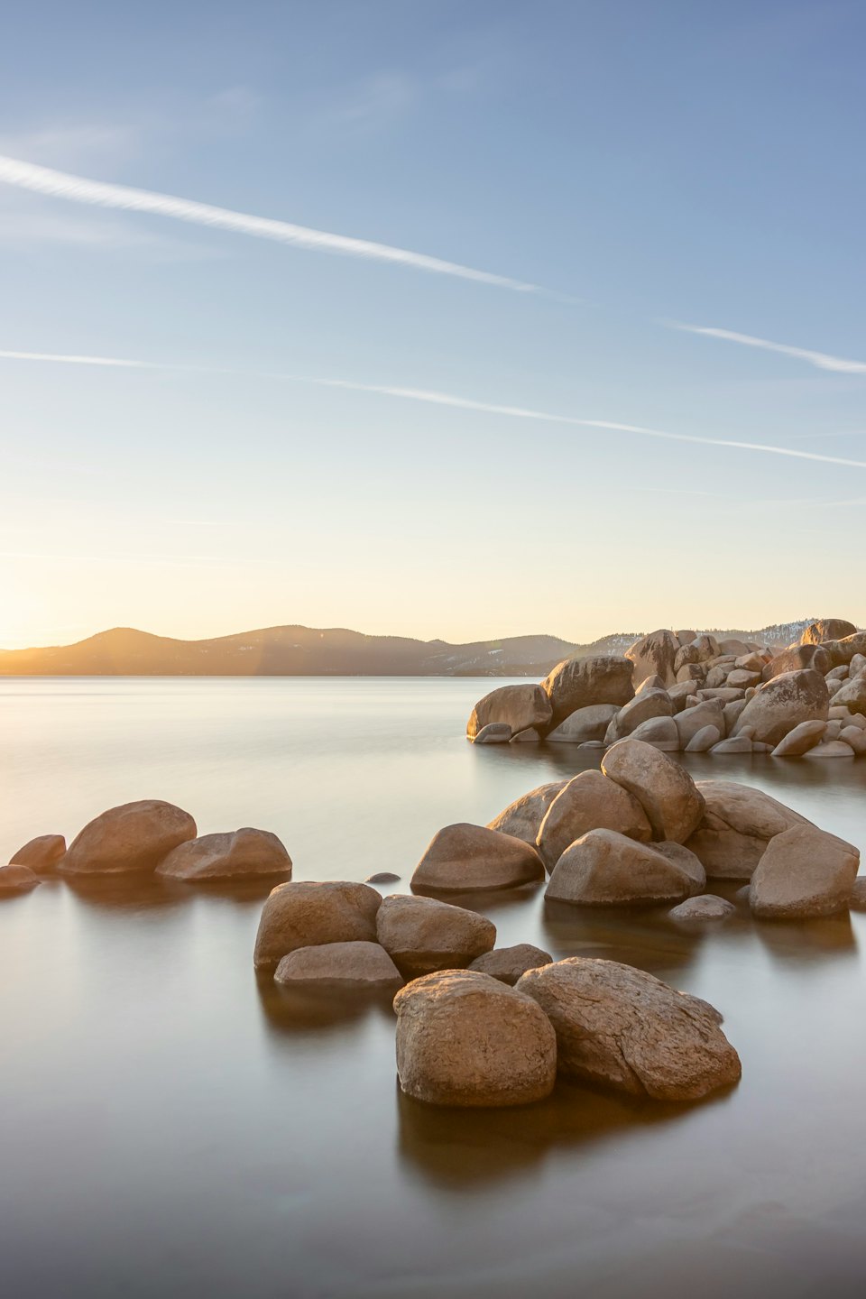 Smooth boulders sit in a calm lake at sunset.
