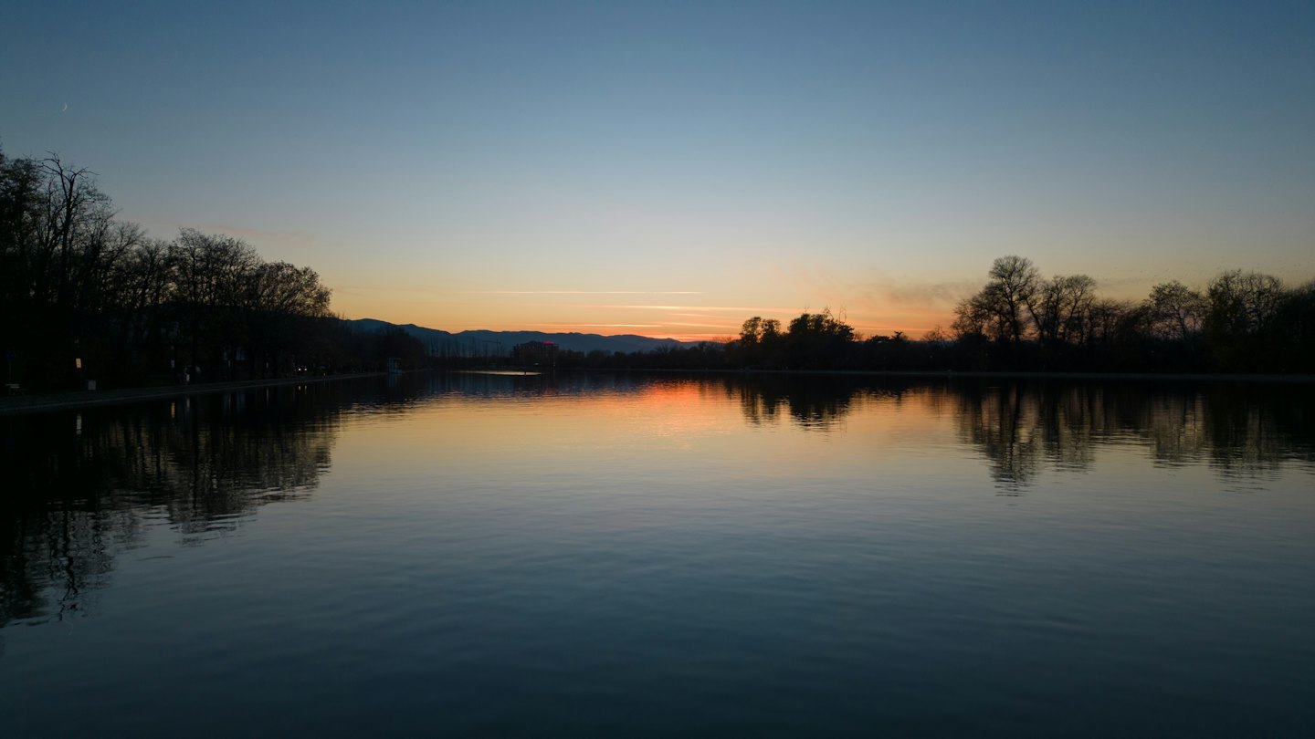 Calm lake at sunset with silhouetted trees.